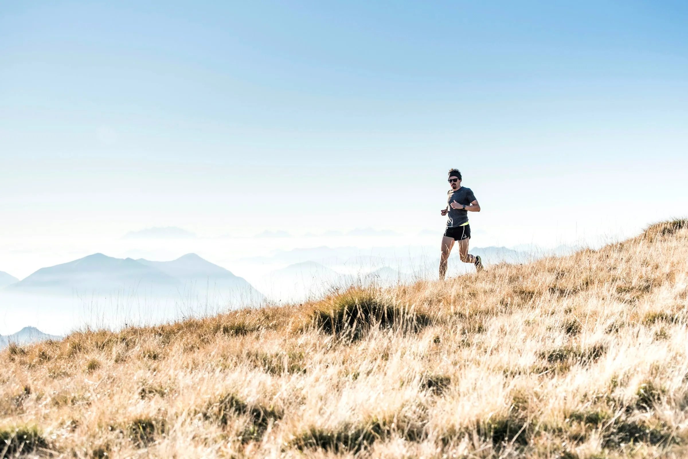 A trail runner on a grassy ridge above the clouds